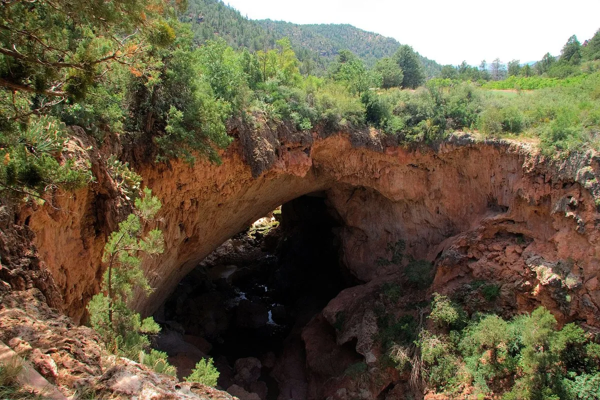 Scenic view of the massive natural travertine arch spanning a lush green canyon at Tonto Natural Bridge, Arizona