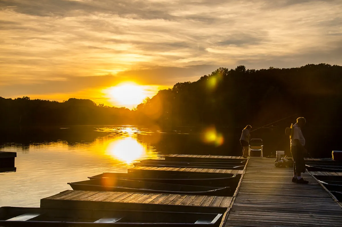 Anglers fishing from a wooden dock at sunset at Chain O' Lakes State Park, Indiana, with rowboats moored alongside