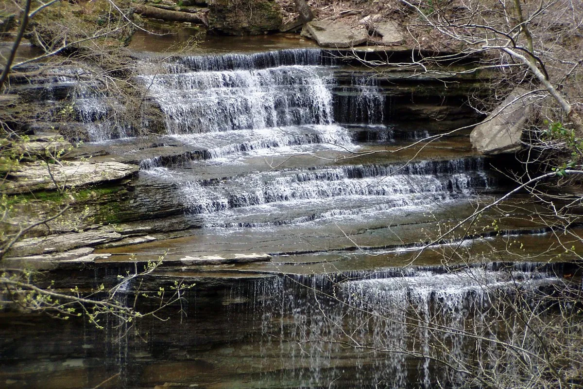 A cascading waterfall tumbling over layered limestone ledges into a forested gorge at Clifty Falls State Park, Indiana