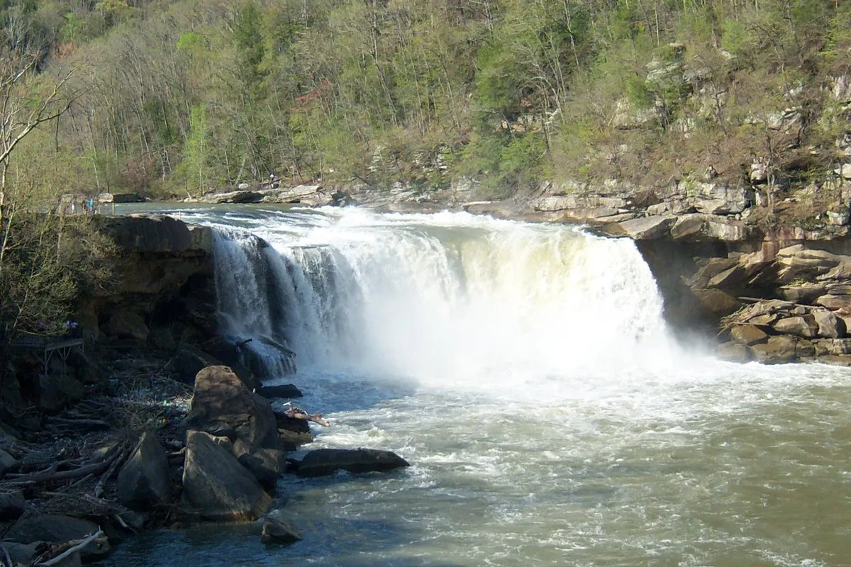 Powerful Cumberland Falls waterfall cascading into the Cumberland River, surrounded by lush forest in Kentucky