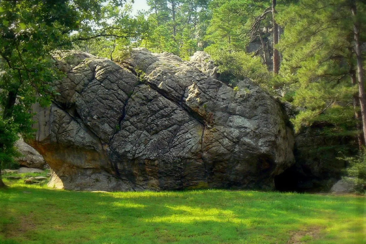 Rugged sandstone cave entrance surrounded by dense green forest at Robbers Cave, Oklahoma