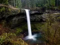 Hiker walking behind a towering waterfall curtain on the Trail of Ten Falls at Silver Falls State Park, Oregon