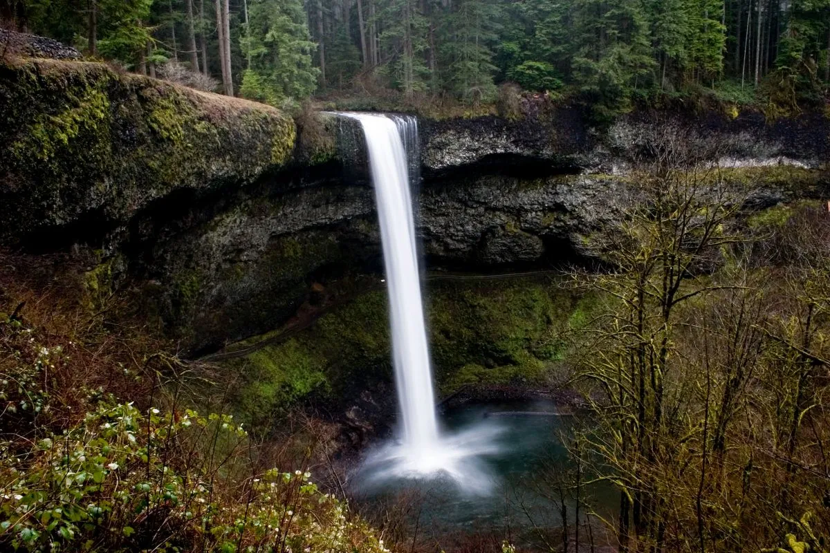 Hiker walking behind a towering waterfall curtain on the Trail of Ten Falls at Silver Falls State Park, Oregon