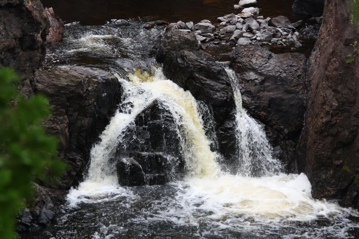 Scenic view of copper-colored waterfalls cascading through a deep lava rock gorge surrounded by dense Northwoods forest at Copper Falls, Wisconsin