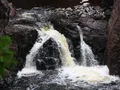 Scenic view of copper-colored waterfalls cascading through a deep lava rock gorge surrounded by dense Northwoods forest at Copper Falls, Wisconsin